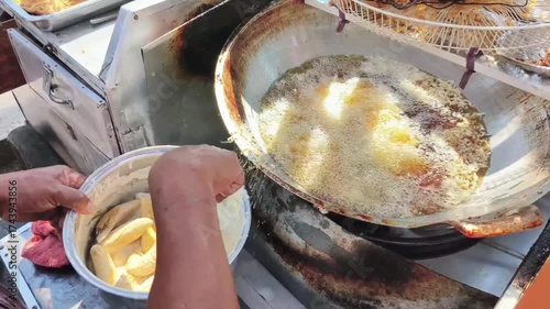 The process of frying bananas by placing batter-dipped bananas into a wok with boiling oil. A popular street food in Indonesia.