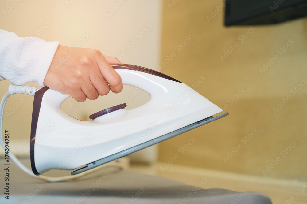 © JK_kyoto - Close-Up of Hand Holding Modern Iron Over Fabric Ready for Pressing and Steam Treatment in Domestic Environment © JK_kyoto - Close-Up of Hand Holding Modern Iron Over Fabric Ready for Pressing and Steam Treatment in Domestic Environment