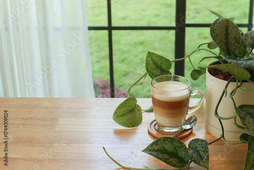 Refreshing cup of iced latte with a small green plant on a wooden table. Warm tones and natural daylight create a relaxing and peaceful mood for interior design and café lifestyle themes.