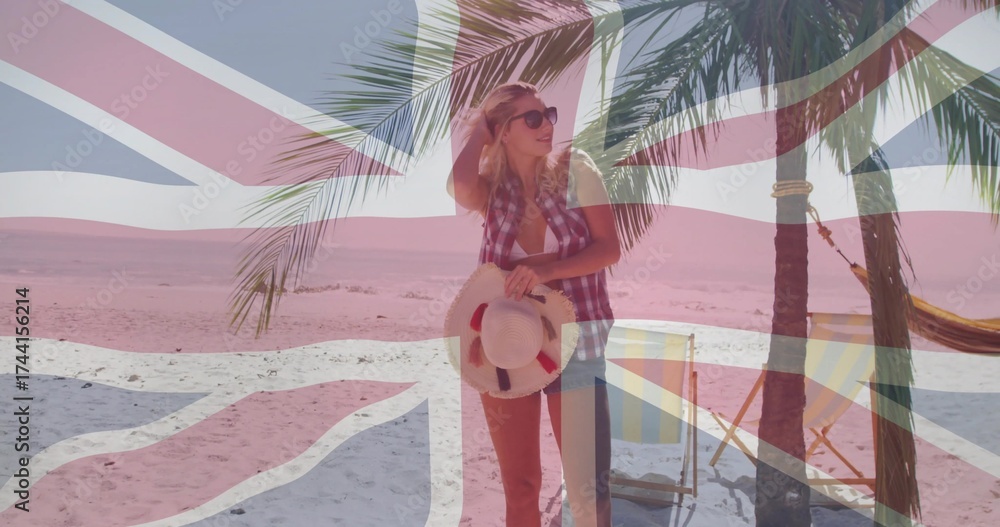 Obraz premium Standing in checkered shirt, shorts on sandy beach, with straw hat, palm tree, Union Jack flag