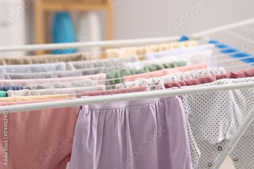 Many clean baby clothes on drying rack indoors, closeup