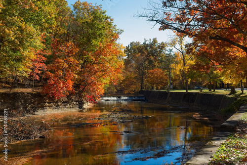 Fototapeta The Rocky River flows over a small spillway amid autumn foliage in Rocky River Reservation, part of the Greater Cleveland Ohio metro parks system