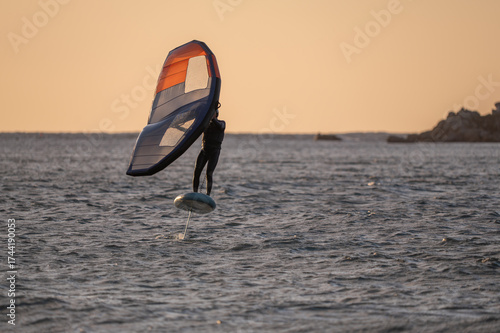 Wingfoiling in Brittany at sunset, a few rocks in the background