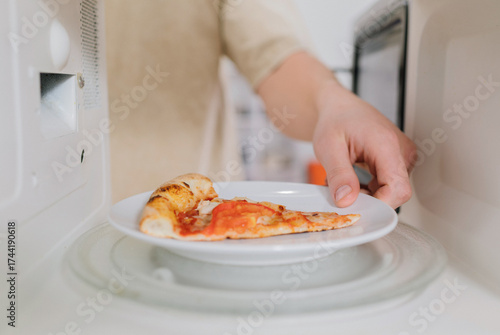 Reheating a slice of leftover pizza on a white plate in a microwave oven.