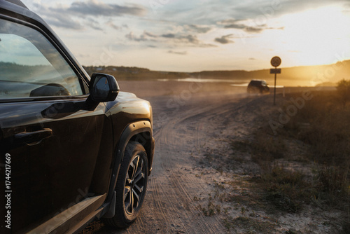 A car is parked on the side of a dirt road during sunset hours