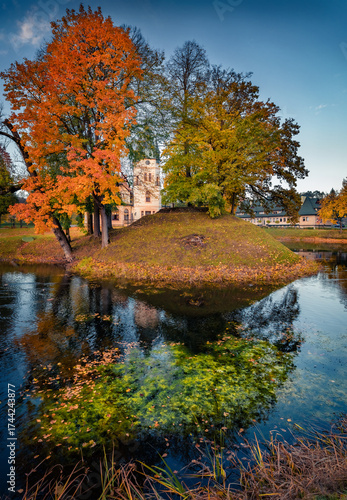 Attractive morning view of Palace Olszanica on the shore of small river. Impressive autumn cityscape of Olszanica town, Poland, Europe. Trees covered with orange and crimson leaves.