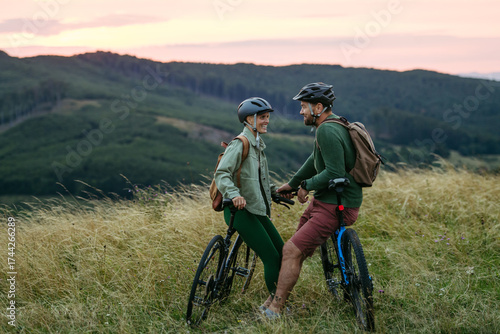 Obraz na plátně Couple cycling together in nature, looking at each other lovingly