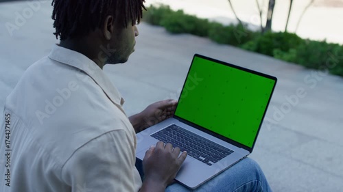 Man using laptop with green screen outdoors