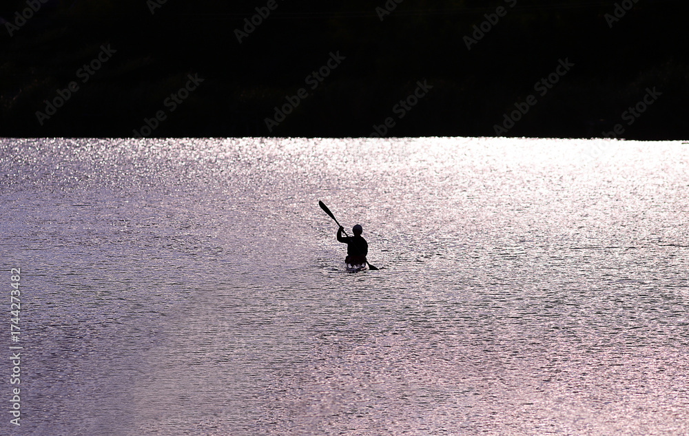 Fototapeta premium A kayaker paddles through the light into the darkness..