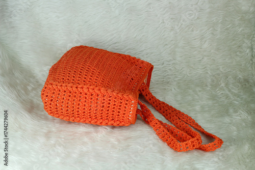 Crocheted handmade orange bag on furry white blanket.