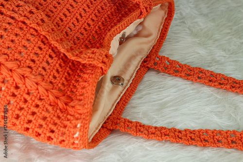 Crocheted handmade orange bag on furry white blanket.