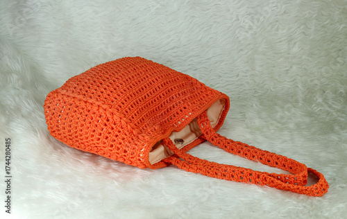 Crocheted handmade orange bag on furry white blanket.