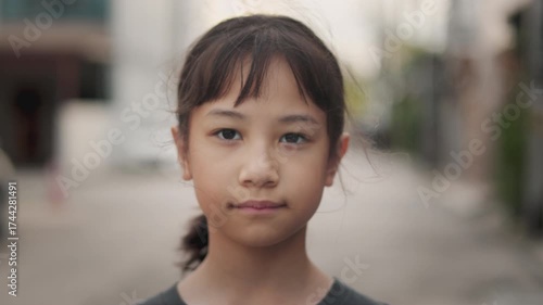 Face focus of Asian kid, a young girl, wearing clear glasses and looking a gentle smile directly to the camera. This shows her innocent, happy expression, positive, reflecting youth and intelligence.