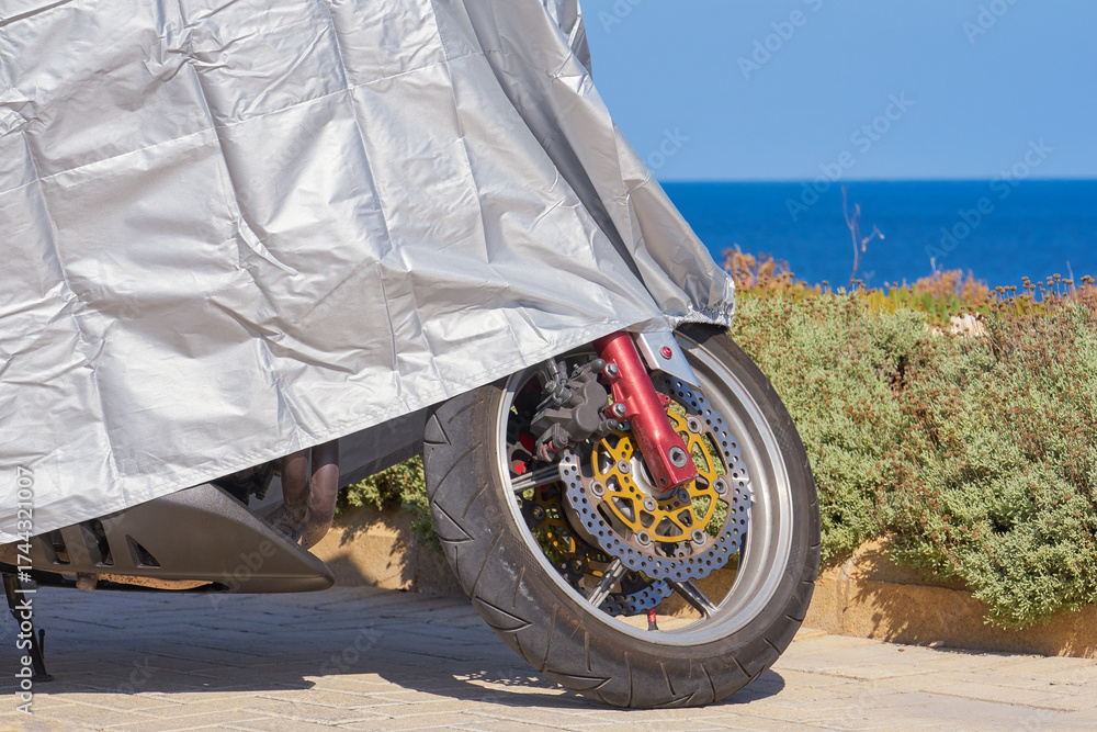 custom made wallpaper toronto digitalDetail of brake disc and tire peeking from silver tarp on parked motorbike near blue sea under bright sky