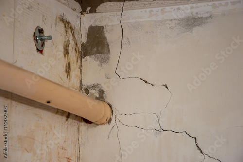 Visible cracks along the wall and ceiling near a plumbing pipe suggest potential problems in the structure of the building