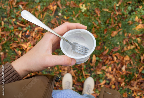 Woman holding a glass with dessert in her hand and eating it with a fork in the park. Quick snack.
