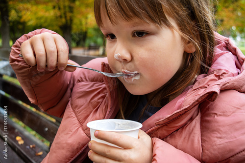 Child sitting on a bench and eating pudding with a fork. Sweet dessert.