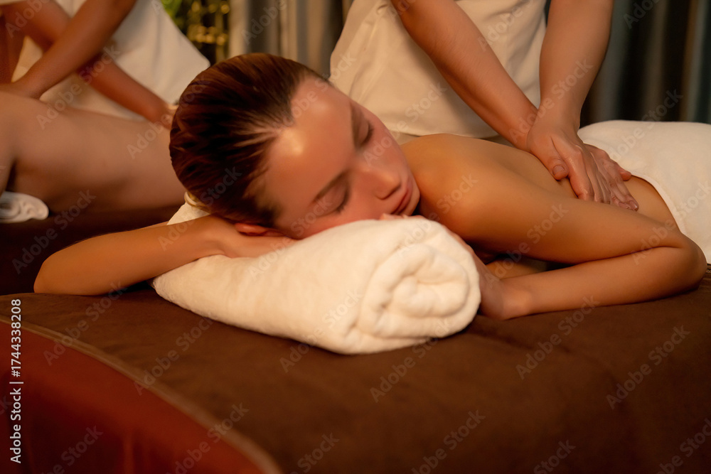 Fototapeta premium Caucasian couple customer enjoying relaxing anti-stress spa massage and pampering with beauty skin recreation leisure in warm candle lighting ambient salon spa at luxury resort or hotel. Quiescent