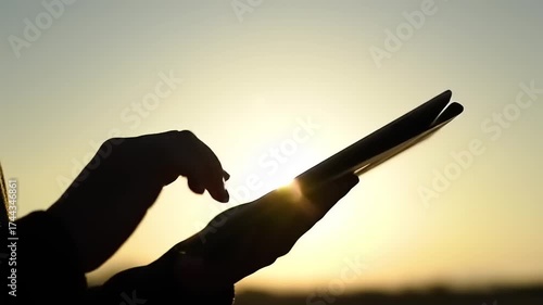 Silhouette of person using tablet at sunset.