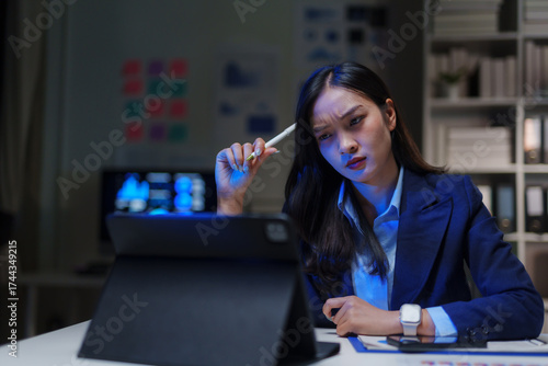 Young Asian businesswoman intensely thinking, working late night in office, dealing with stress and complex business problems