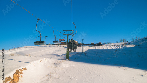 Empty Cable Car Cabins Moving Above Deep Snow with Distant Smoking Chalet in Serene Winter Ski Resort Landscape