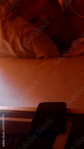 Vertical video. Woman Reaching from Bed to Stop 5 AM Alarm on Smartphone Then Looking Out the Window at Bright Morning and Lying Back Sleepy Morning Routine