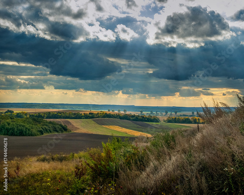 Landscape with fields on the horizon, sun rays through dramatic clouds