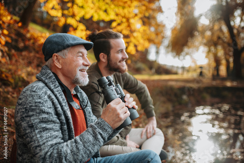Senior father and his son with binoculars in nature, talking.