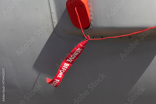 Remove before flight - safety warnign red ribbon and tag. Detail of airplane, plane. Safety procedure in aviation and aeronautics.