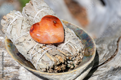 Heart shaped carnelian crystal and two white sage smudge sticks. 