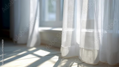 A sheer white curtain sways in the breeze by a sunlit window. Morning sunlight casts shadows on a wooden floor. Cozy home interior and new day concept