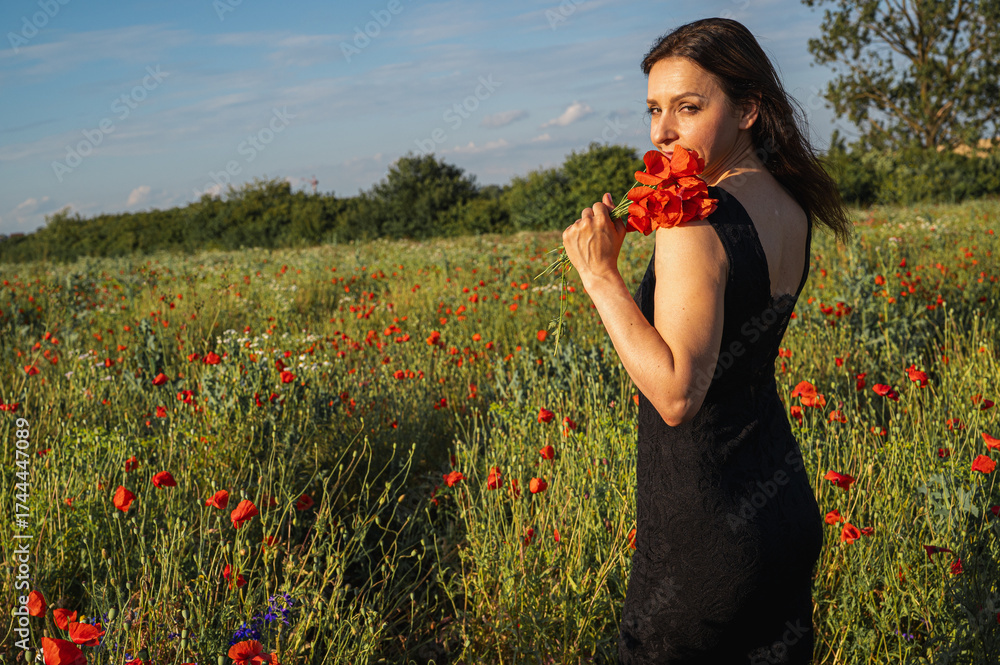 Φωτογραφία Woman in a black dress gracefully holding vibrant red poppies in a sunlit field, embodying freedom, natural beauty, and summer joy