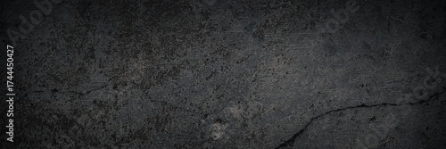 Texture of old cracked concrete wall. Rough dark gray concrete surface with spots, cracks, noise and grain. Dark wide panoramic background for design. Shaded texture with vignette.
