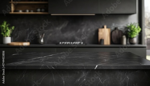 The image shows a black marble countertop in a modern kitchen with dark cabinetry and a blurred background of kitchen utensils and plants.