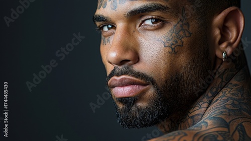 Captivating portrait of a man showcasing intricate tattoos against a dark background in a studio setting