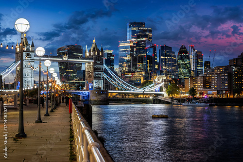 Beautiful evening view from the Thames River walkway to the illuminated Tower Bridge and City of London, England