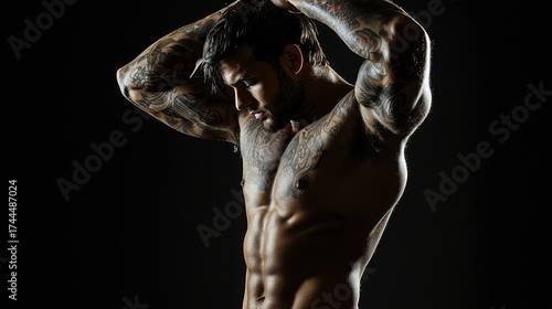 Muscular man with tattoos posing under dramatic lighting, showing strength and confidence in a studio setting