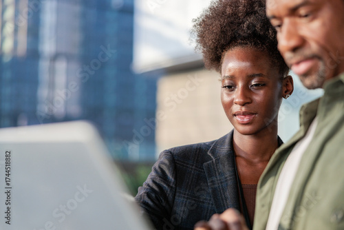 Business colleagues review laptop in front of city building.