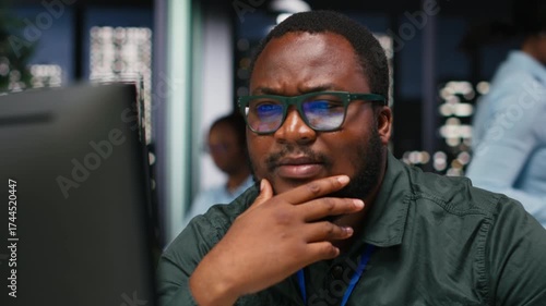 African american analyst wondering about possible solutions to a dilemma on computer, concentration to evaluate projections with logical deduction and intuitive observation at night. Camera B.