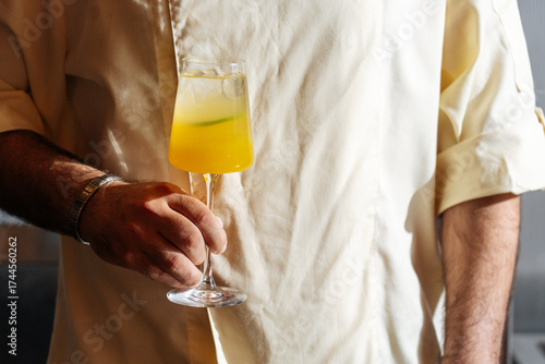Man holding yellow cocktail in stemmed glass 