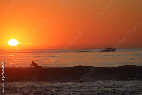 silhouette of a surfer and boat with sunrise background