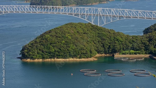 高台の展望台から広大な海に架かる白いトラス橋と手前の養殖場を捉えた固定ショットフッテージ