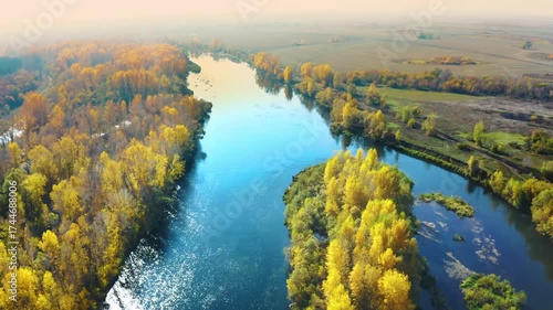 An aerial drone shot captures the serene beauty of the Agidel River, also known as the Belaya River, as it winds through a vibrant autumn landscape in the South Ural region of Russia. The footage show