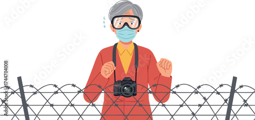 An elderly person wearing protective gear stands behind barbed wire with a camera.