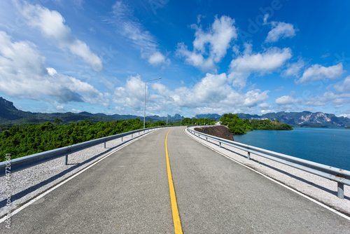 Asphalt road on the dam with blue sky and cloud background.