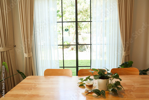 Bright dining table by large window with sunlight and indoor plants. Scandinavian style home interior with natural wood furniture.