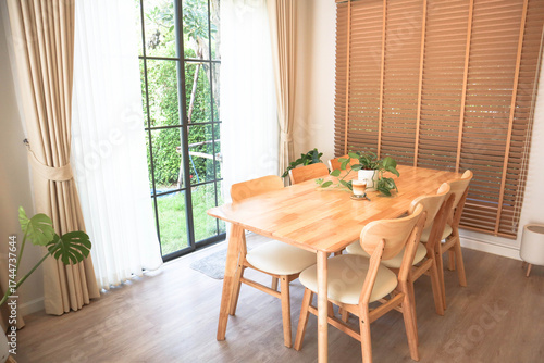 Modern dining room with natural wooden table, indoor plants, and sunlight through large glass windows. Warm Scandinavian interior for cozy home inspiration.
