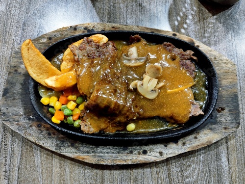 Close-up of juicy beef steak with mushroom sauce and vegetables on a wooden table, perfect for restaurant or food menu concept