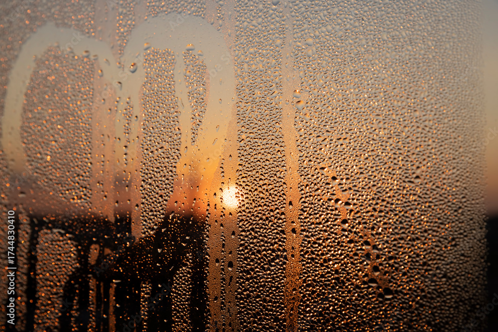 Obraz premium condensation on the window glass at sunset, wet glass with lots of water droplets on the background of an orange sky