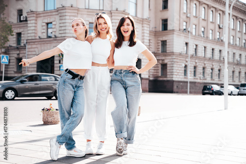 Three young beautiful smiling hipster female in trendy summer white t-shirt  and jeans clothes. Sexy carefree women posing in the street. Positive models having fun, going crazy. In sunny day